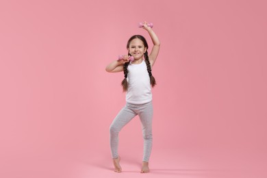 Cute little girl with dumbbells on pink background