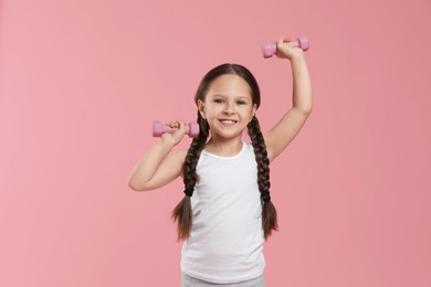 Photo of Cute little girl with dumbbells on pink background