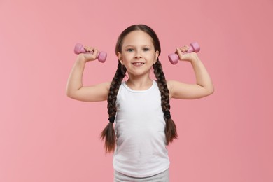 Cute little girl with dumbbells on pink background