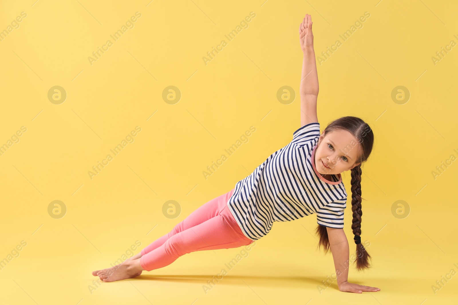 Photo of Cute little girl doing gymnastic exercise on yellow background, space for text