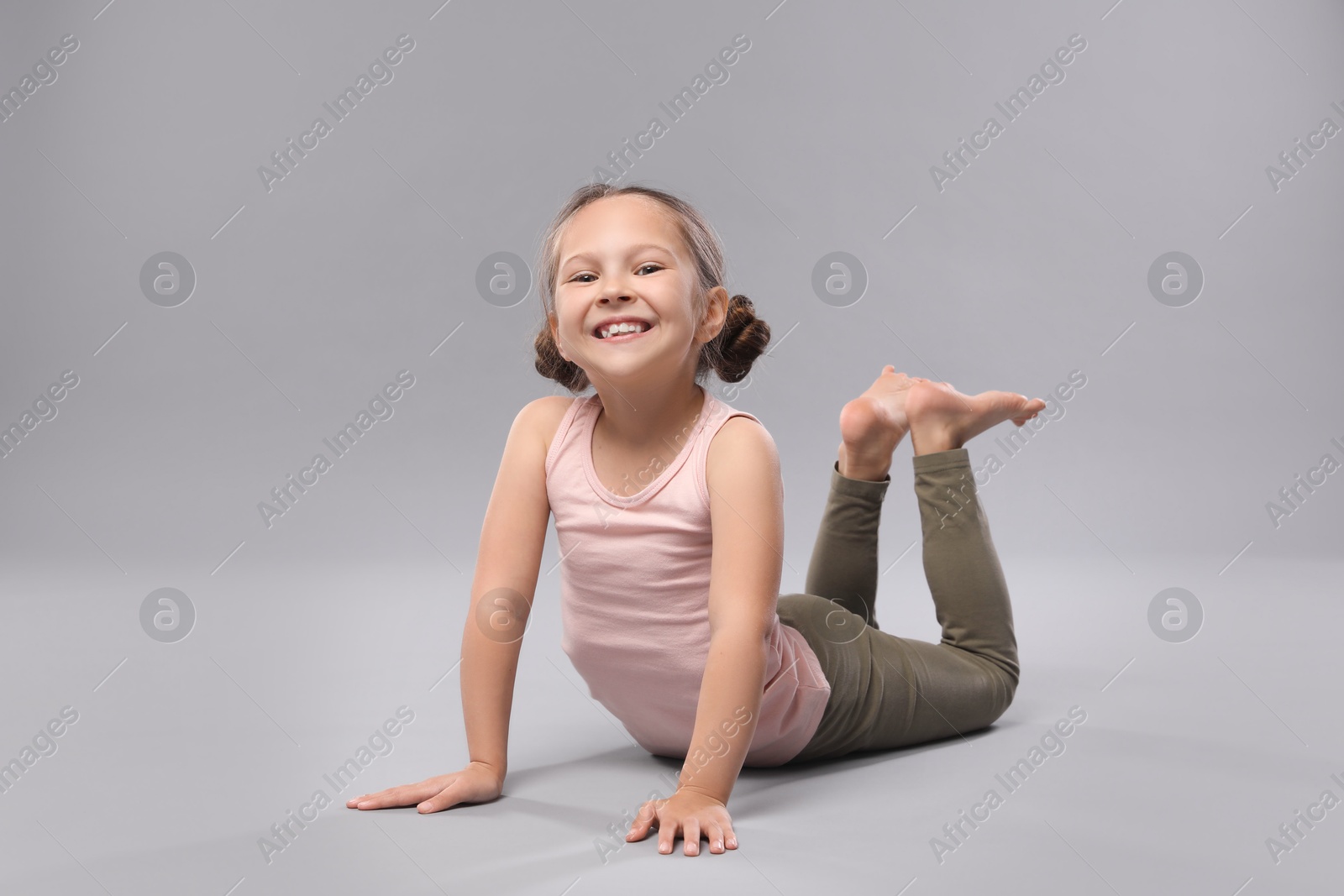 Photo of Cute little girl doing gymnastic exercise on grey background