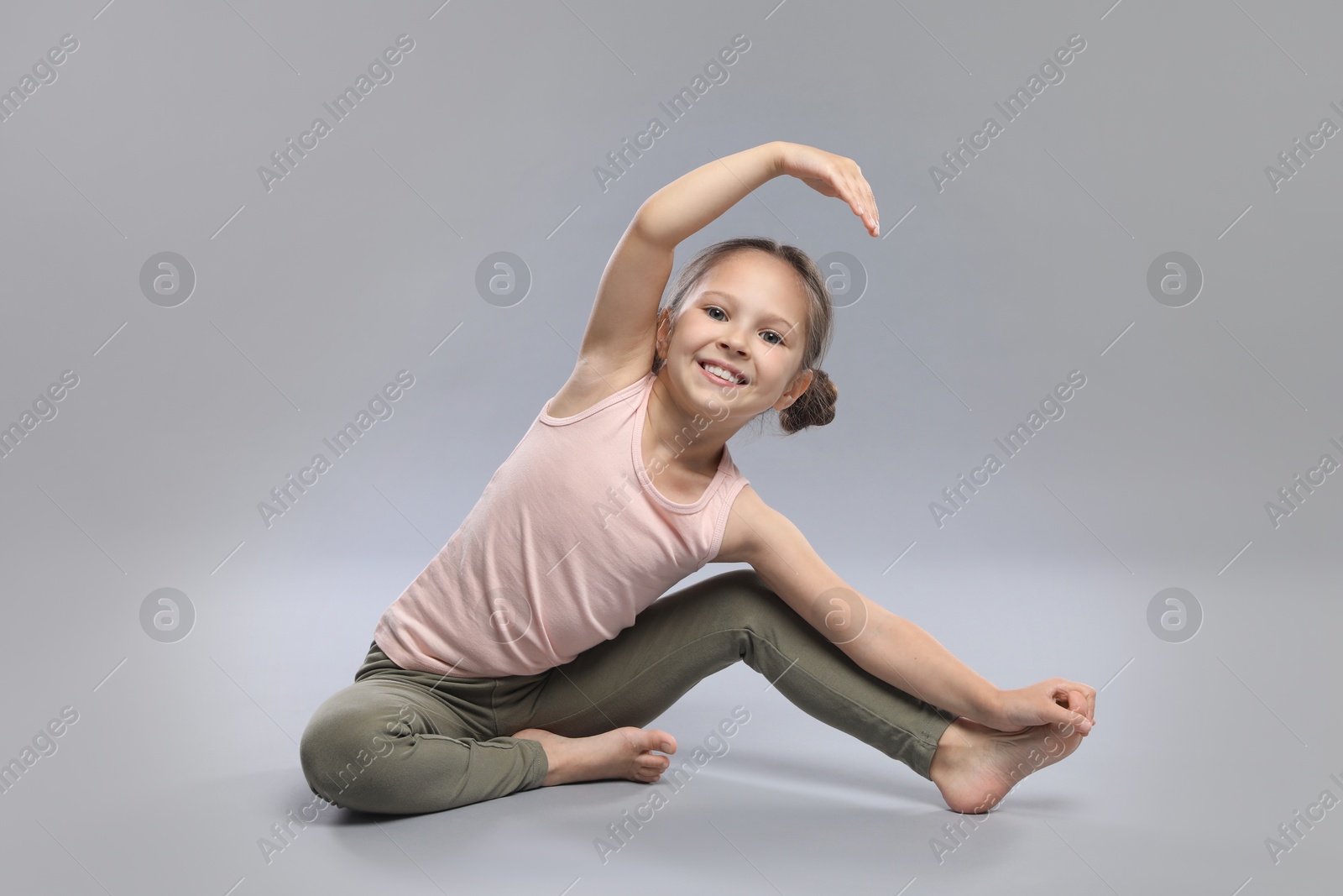 Photo of Cute little girl stretching on grey background