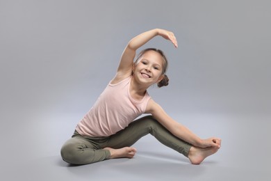 Cute little girl stretching on grey background