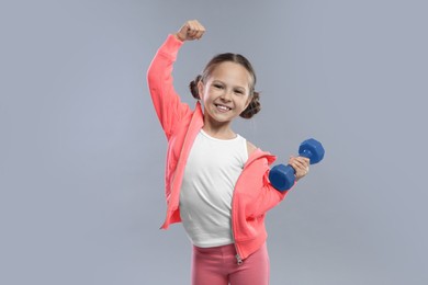 Cute little girl with dumbbell on grey background