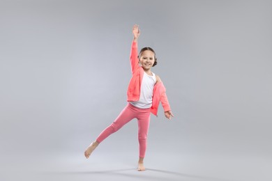 Cute little girl doing gymnastic exercise on grey background