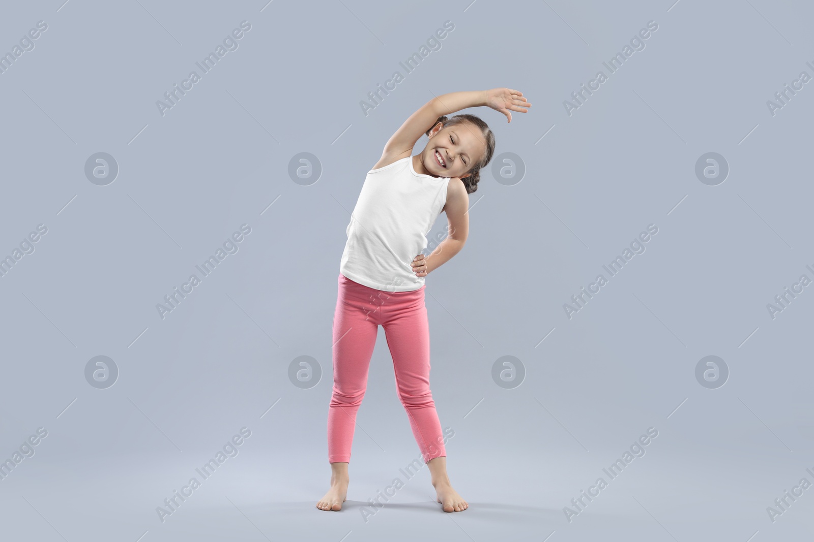 Photo of Cute little girl stretching on grey background