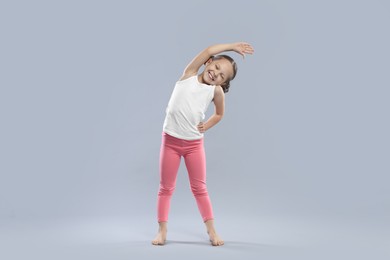 Cute little girl stretching on grey background