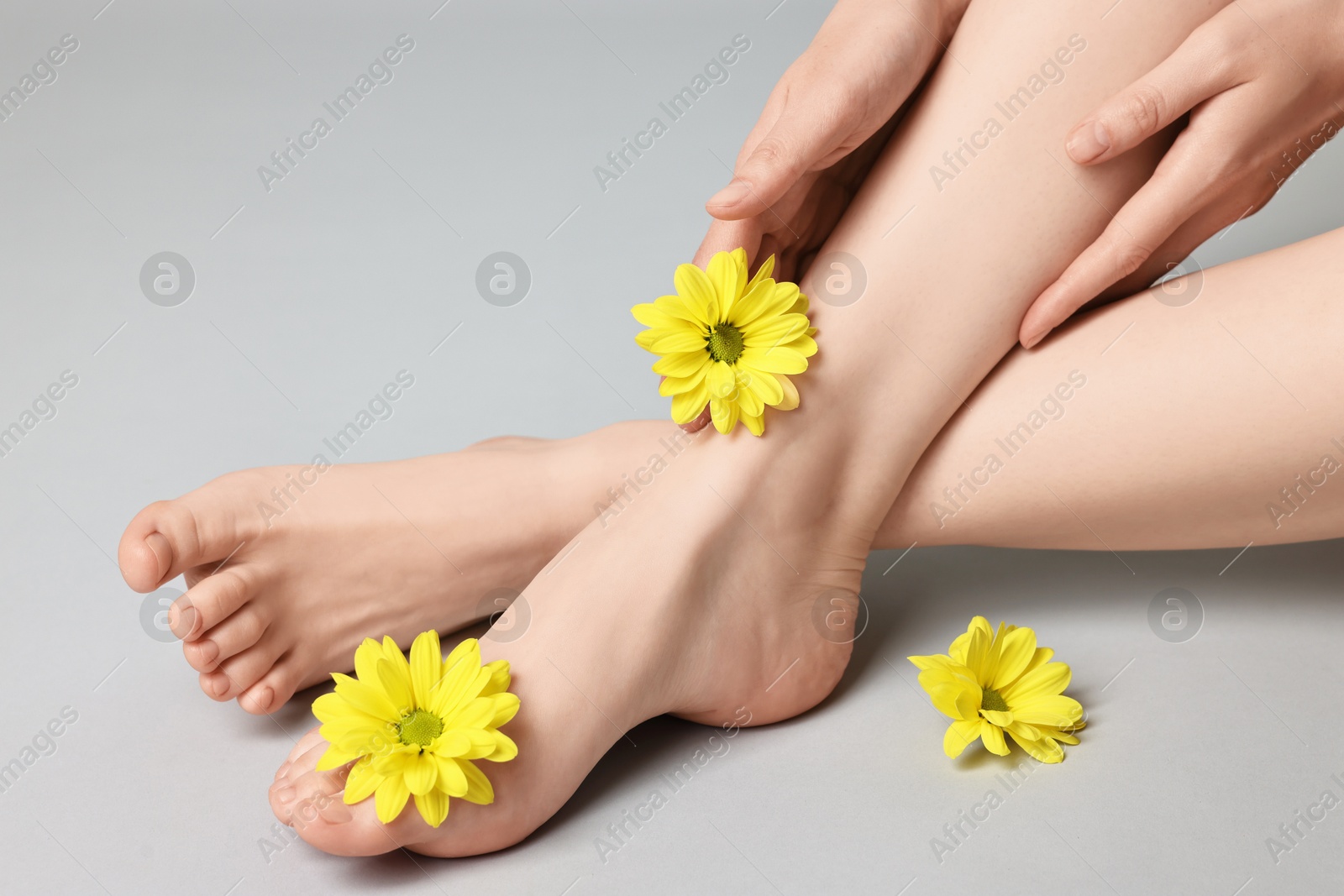 Photo of Closeup view of woman`s groomed feet after care procedure and beautiful flowers on grey background