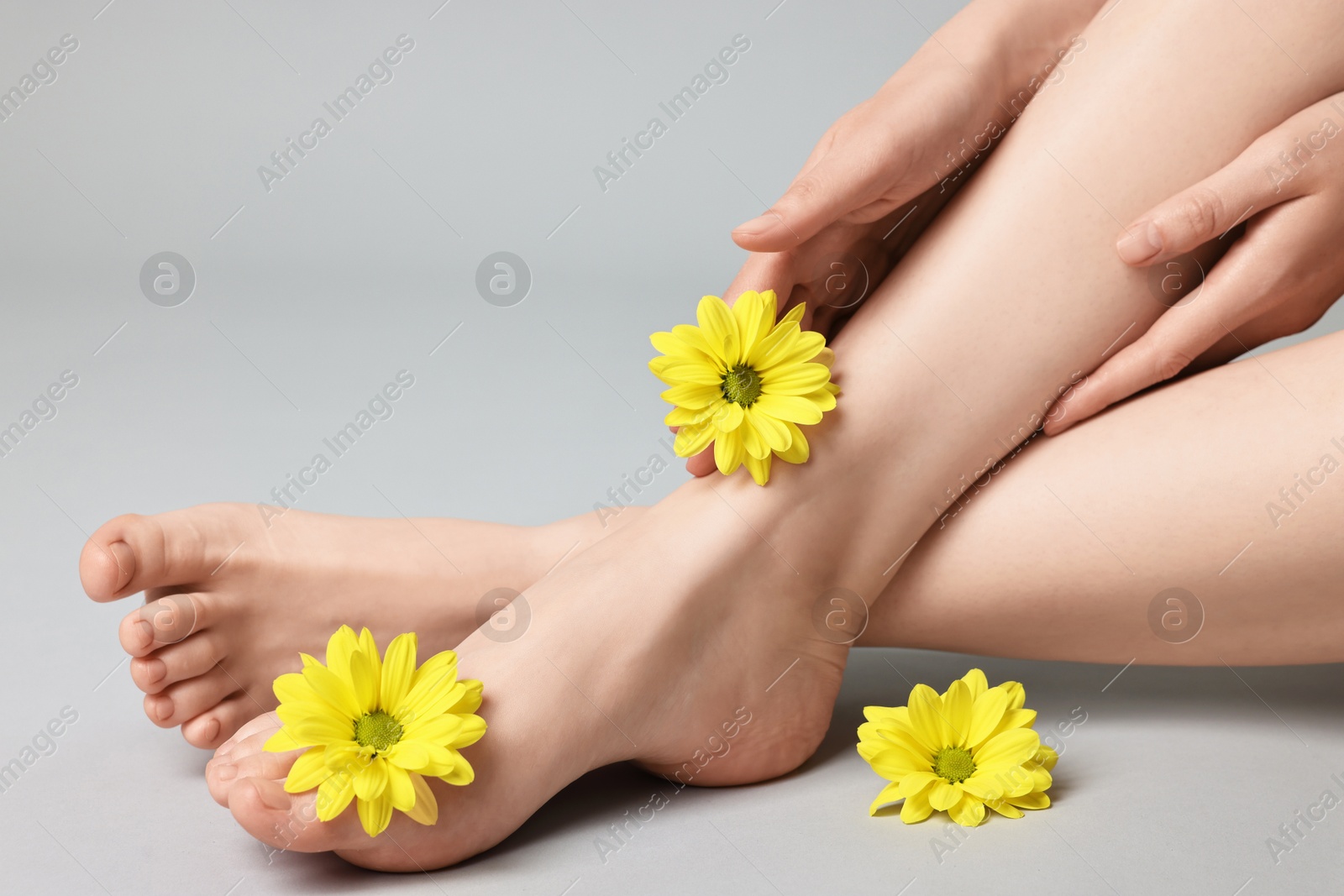 Photo of Closeup view of woman`s groomed feet after care procedure and beautiful flowers on grey background