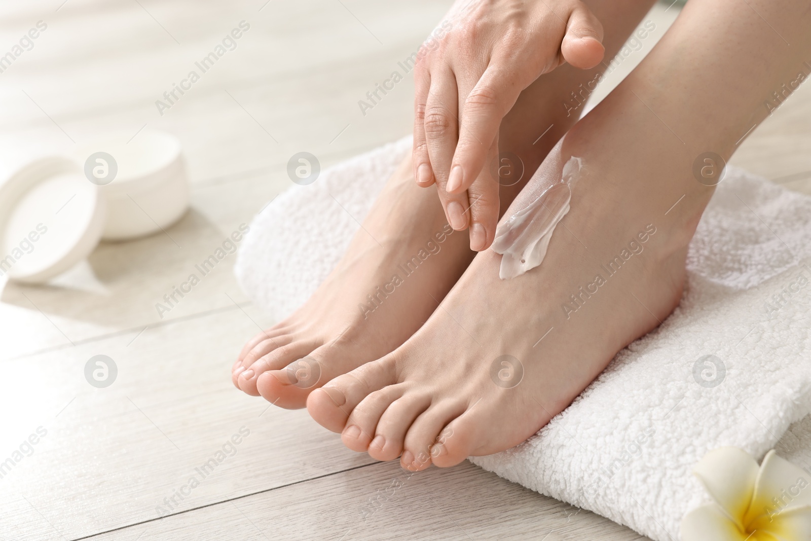 Photo of Woman applying moisturizing cream onto her feet on floor, closeup. Body care