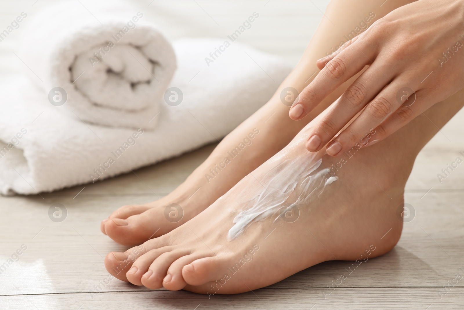 Photo of Woman applying moisturizing cream onto her feet on floor, closeup. Body care