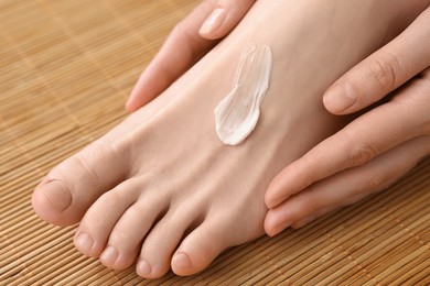 Photo of Woman applying moisturizing cream onto her foot on bamboo mat, closeup. Body care