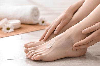 Photo of Woman applying moisturizing cream onto her feet on floor, closeup. Body care