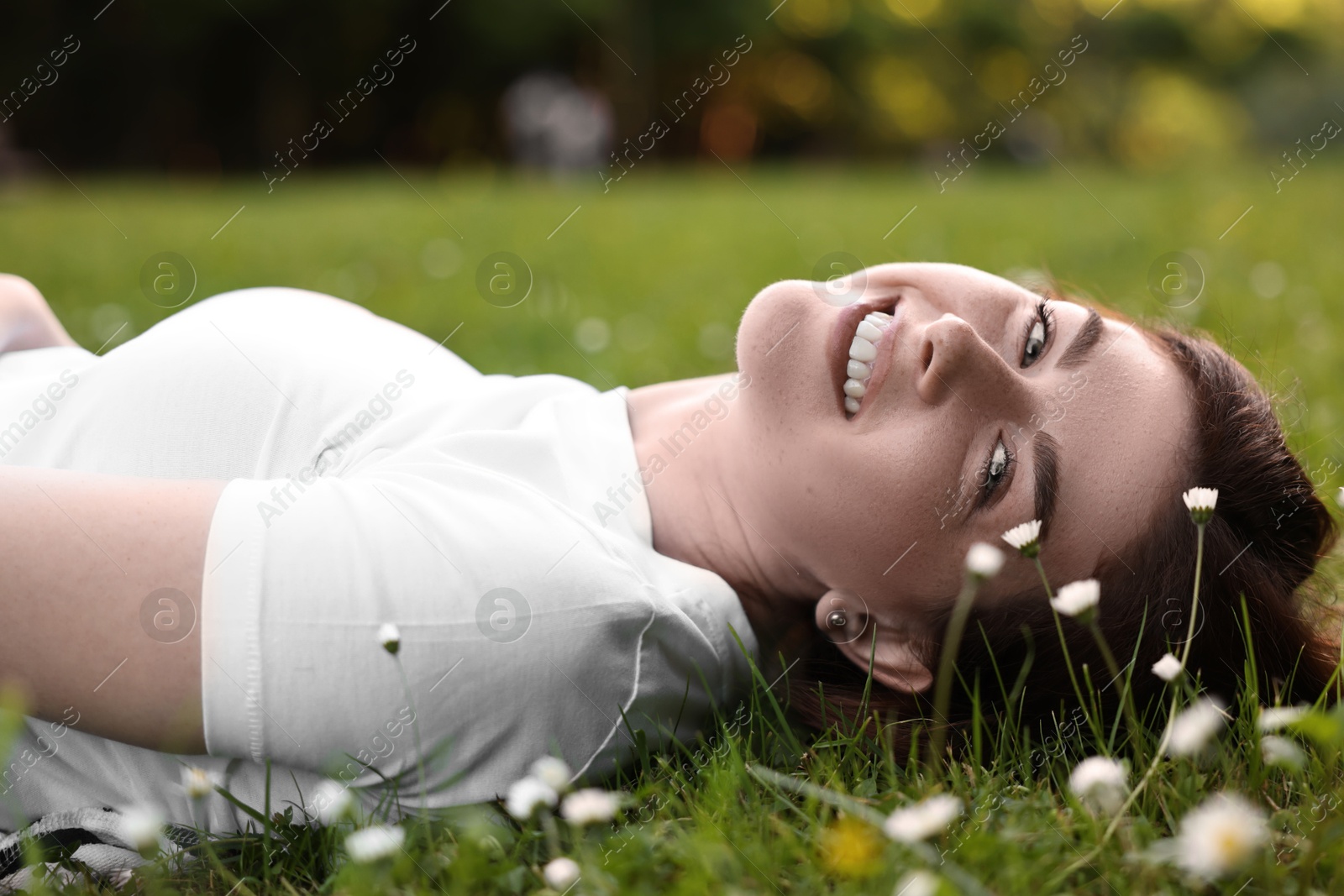 Photo of Portrait of smiling woman lying on grass and flowers. Spring vibes