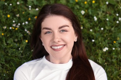 Portrait of smiling woman lying on grass and flowers, top view. Spring vibes