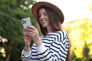 Photo of Portrait of smiling woman in hat with smartphone outdoors. Spring vibes