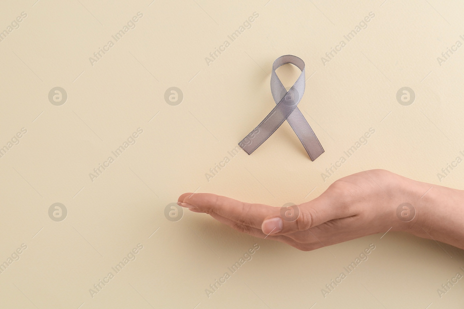 Photo of Woman with grey awareness ribbon on beige background, top view. Space for text