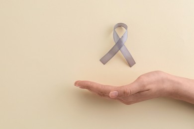 Woman with grey awareness ribbon on beige background, top view. Space for text