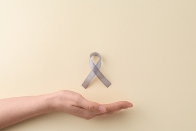 Photo of Woman with grey awareness ribbon on beige background, top view. Space for text