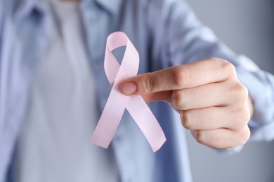 Woman with pink awareness ribbon on grey background, closeup