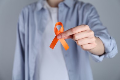 Woman with orange awareness ribbon on grey background, closeup