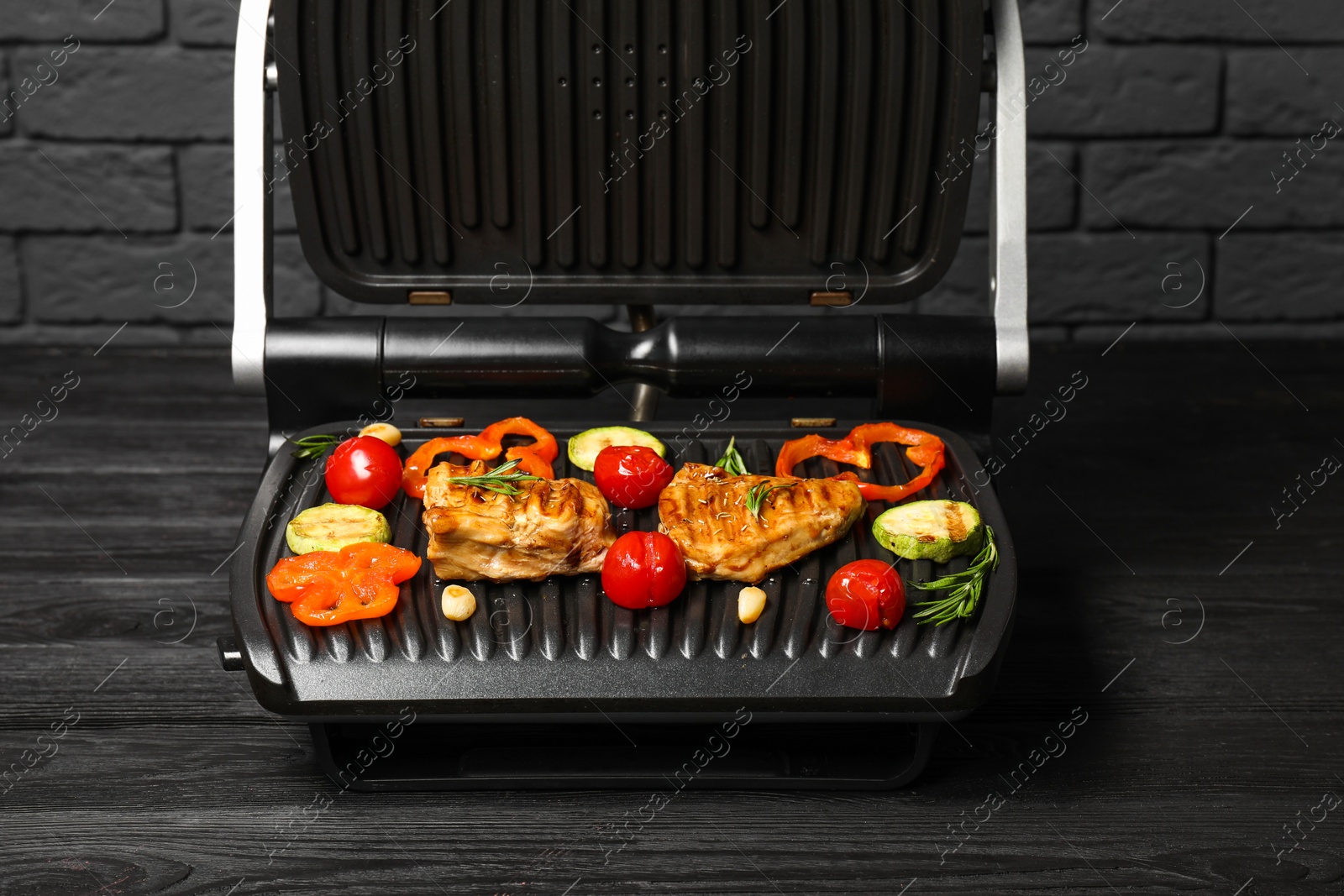 Photo of Electric grill with tasty meat, spices and vegetables on black wooden table