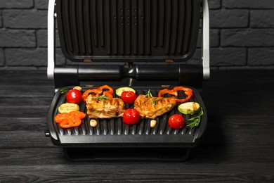 Photo of Electric grill with tasty meat, spices and vegetables on black wooden table