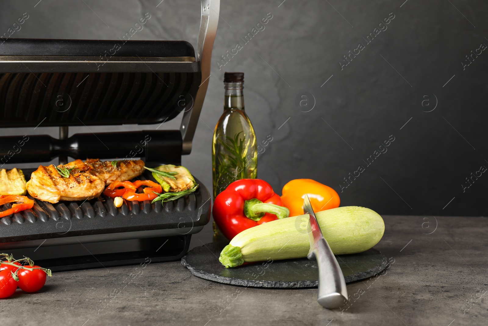 Photo of Electric grill with different products and knife on grey textured table