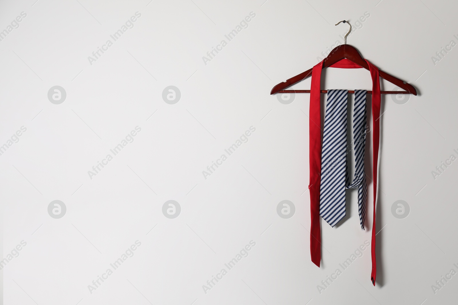 Photo of Hanger with different stylish neckties on light wall. Space for text