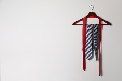 Photo of Hanger with different stylish neckties on light wall. Space for text