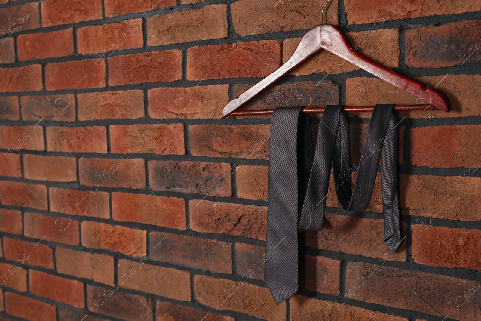 Photo of Hanger with black necktie on red brick wall. Space for text