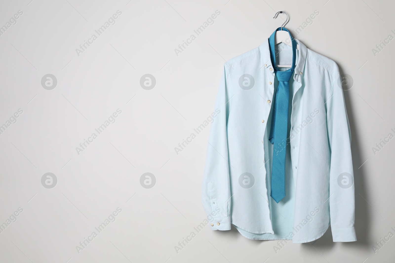 Photo of Hanger with stylish shirt and turquoise necktie on light wall, space for text