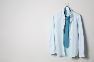 Hanger with stylish shirt and turquoise necktie on light wall, space for text