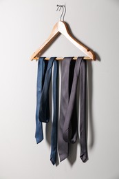 Hanger with different stylish neckties on light wall