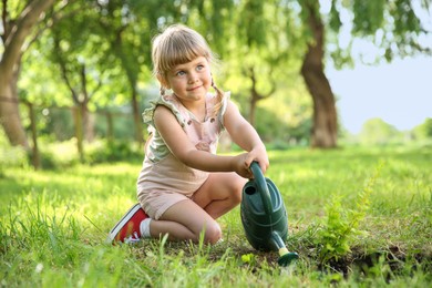 Cute little girl watering tree in garden