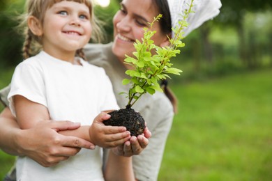 Mother and her daughter planting tree together in garden, space for text