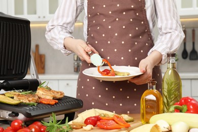 Woman cooking different products with electric grill at wooden table in kitchen, closeup