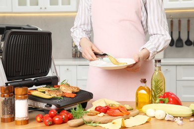 Photo of Woman cooking different products with electric grill at wooden table in kitchen, closeup