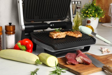 Photo of Electric grill and different products on white wooden table, closeup