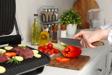 Woman cooking different products with electric grill at white wooden table in kitchen, closeup