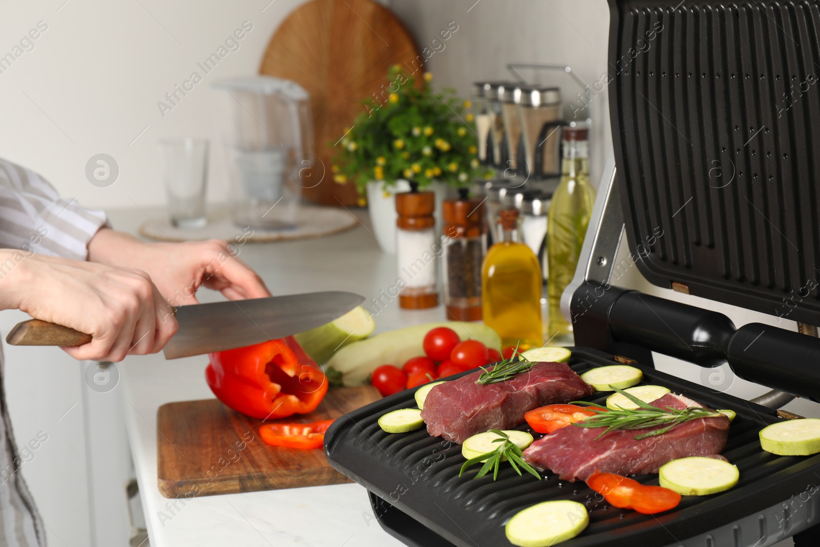 Photo of Woman cooking different products with electric grill at white wooden table in kitchen, closeup