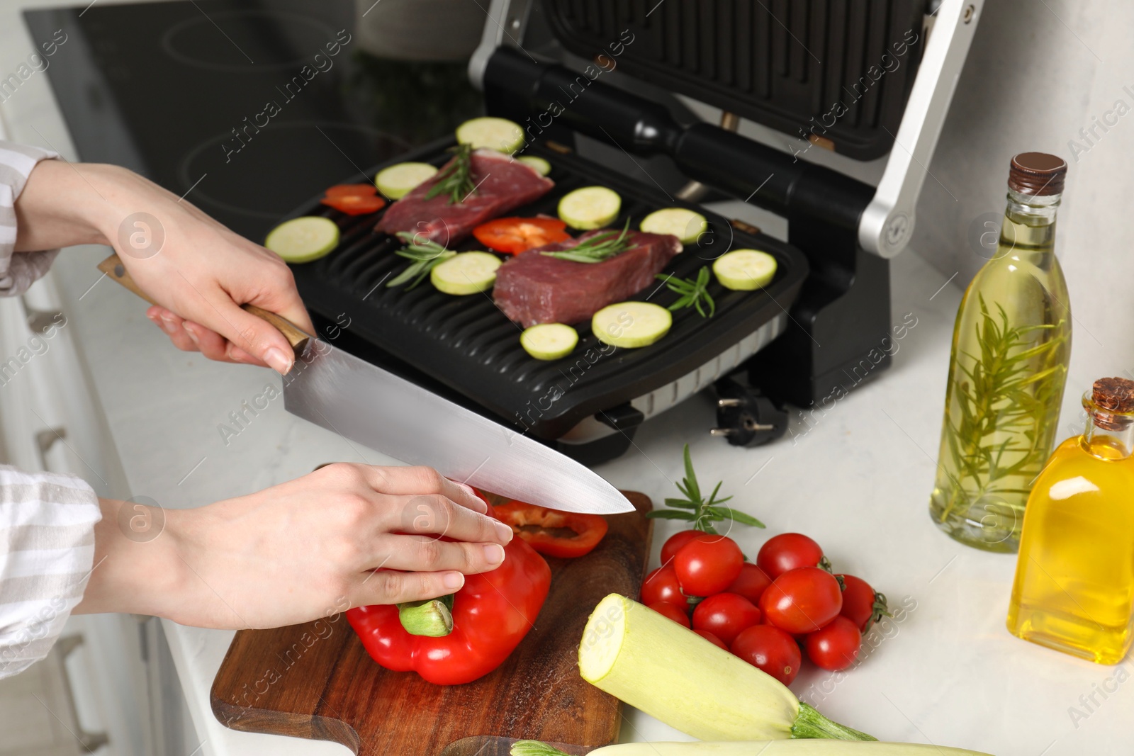 Photo of Woman cooking different products with electric grill at white wooden table in kitchen, closeup