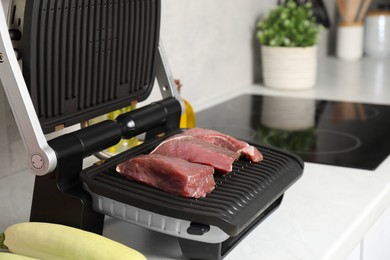 Photo of Electric grill, meat and zucchini on white wooden table