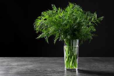 Photo of Fresh dill in glass on grey textured table against black background. Space for text