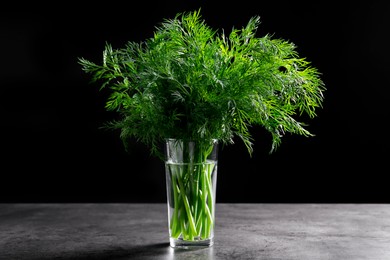 Photo of Fresh dill in glass on grey textured table against black background, closeup