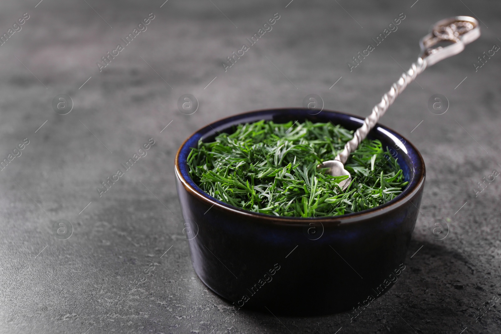 Photo of Fresh cut dill and spoon in bowl on grey textured table, closeup. Space for text