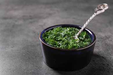 Fresh cut dill and spoon in bowl on grey textured table, closeup. Space for text