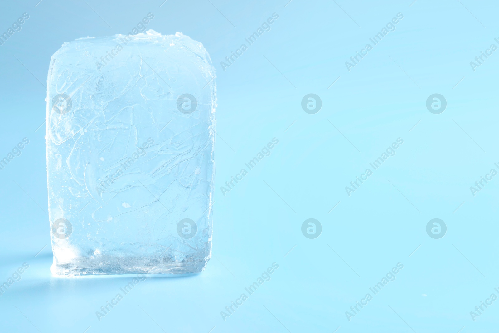 Photo of Cube of clear ice on light blue background, space for text