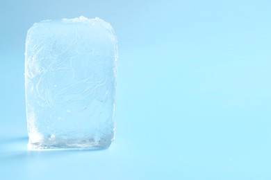 Cube of clear ice on light blue background, space for text