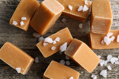 Photo of Yummy caramel candies with sea salt on wooden table, flat lay